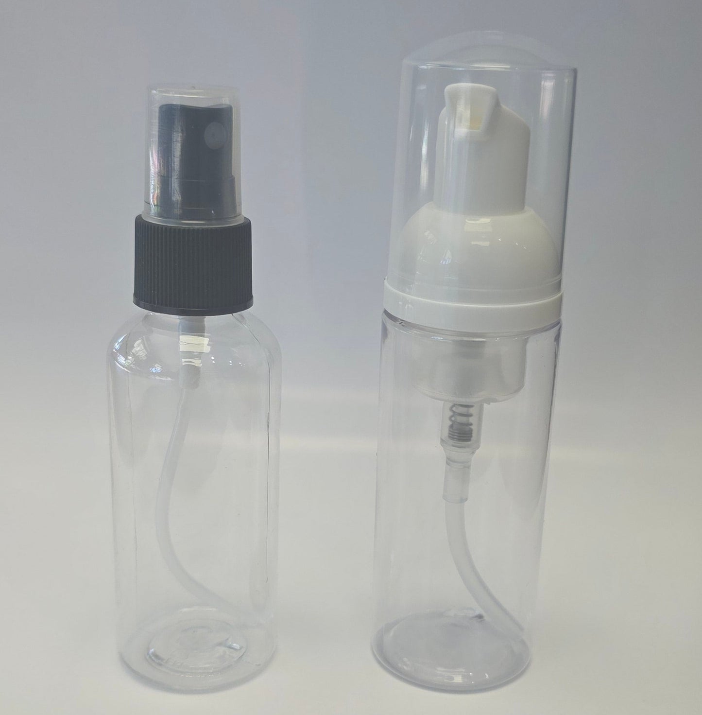 Two bottles, one is a clear plastic spray bottle with black cap and the other is a clear plastic foaming pump bottle with a white pump on a light gray background